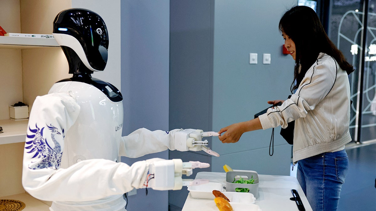 A woman touches the hand of a humanoid robot.