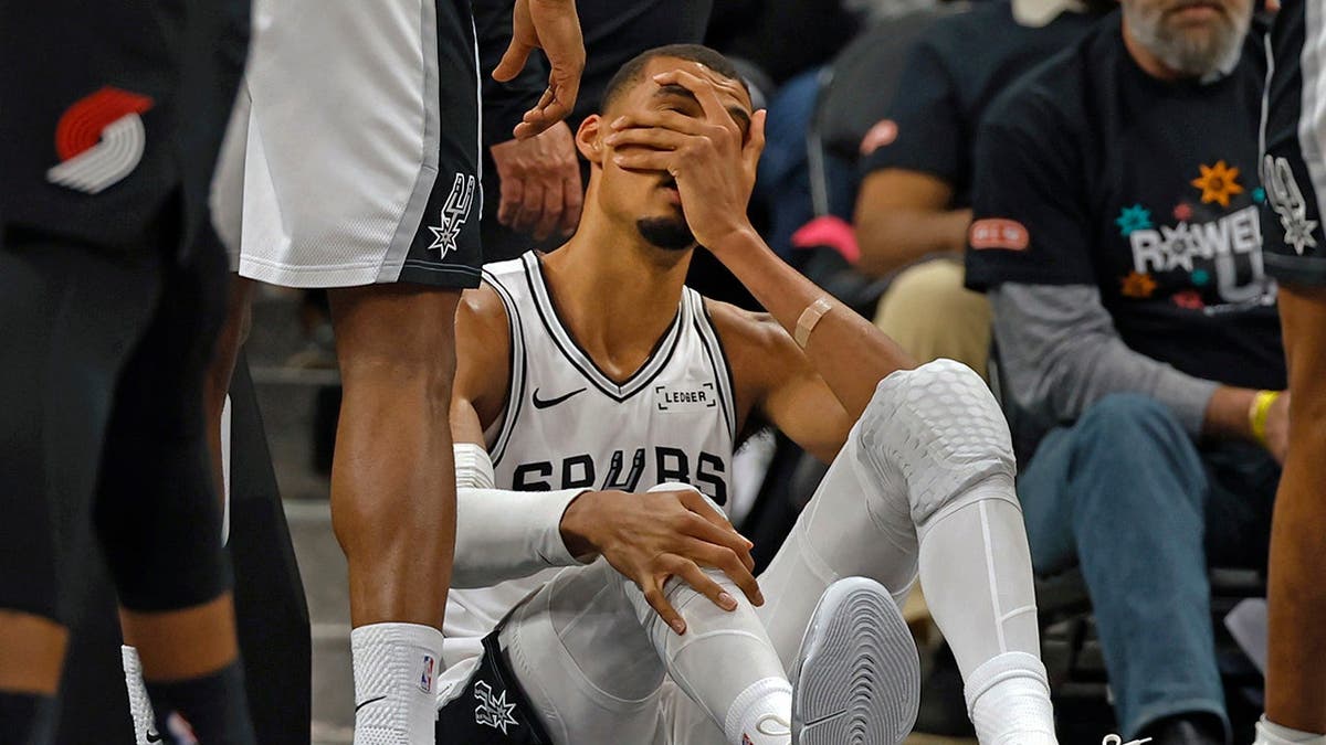 Victor Wembanyama holding his head after falling on the basketball court.
