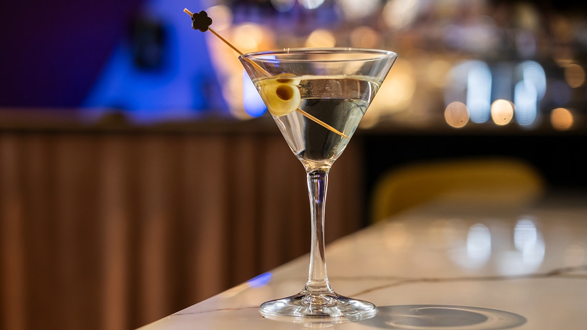 Martini with olives in stemmed glass on bar.