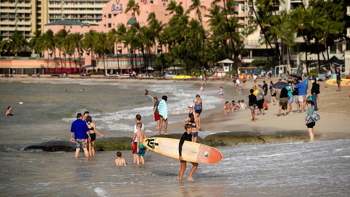 Visitors playing on Waikiki Beach in Honolulu with waves and cloudy sky