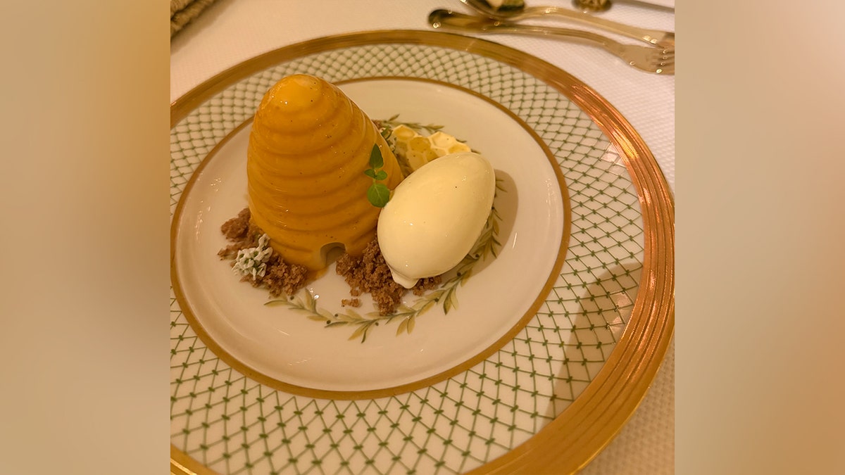 Honeycomb-shaped dessert with almond joconde sponge, served with crème fraîche ice cream and White House honey on an elegant patterned plate.
