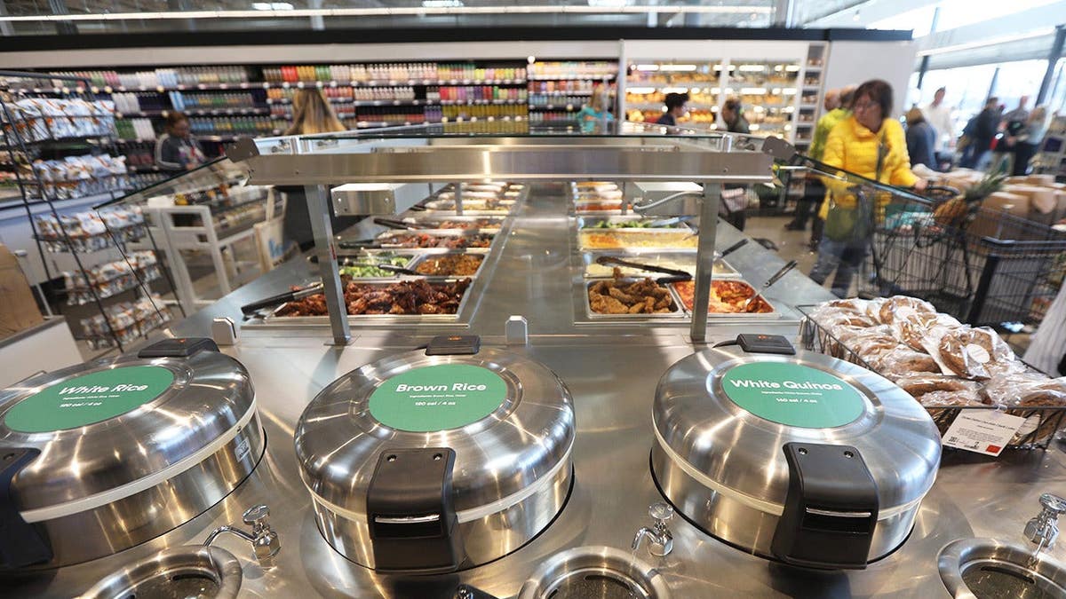 Hot food bar seen in Whole Foods grocery store as customers walk past.