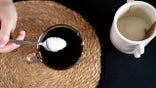 Person pouring sweetener in black coffee seen from overhead angle.
