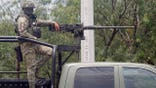 A member of the Mexican Army standing guard on the back of a truck.