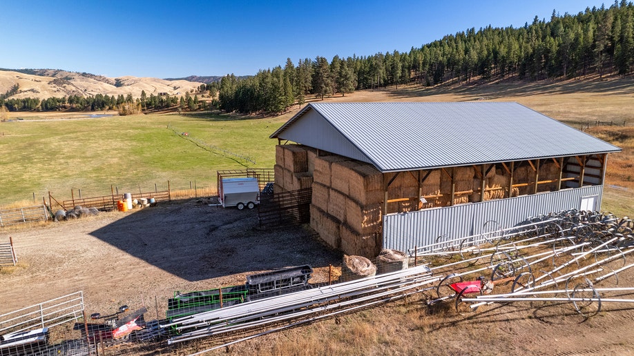 Hay barn with farming equipment and fenced pasture at ranch