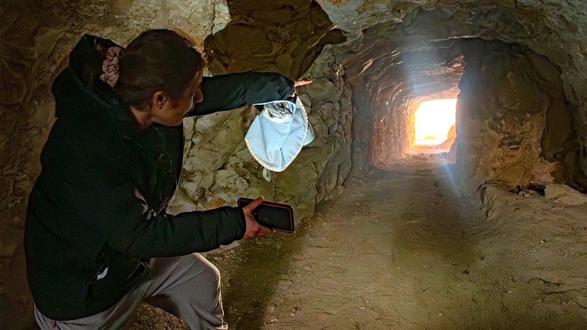 Arqueólogo com máscara apontando para túnel