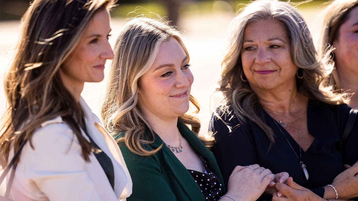 Abigail Zwerner smiles with her parent Julie arsenic her lawyers talk to members of the press