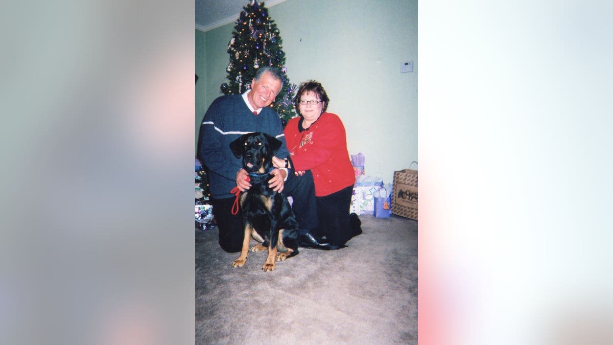 Jeff Walton and Deb Proctor smiling in front of a Christmas tree for a holiday portrait holding onto their dog.