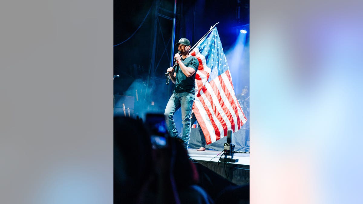 Granger Smith holding a large American flag on stage.