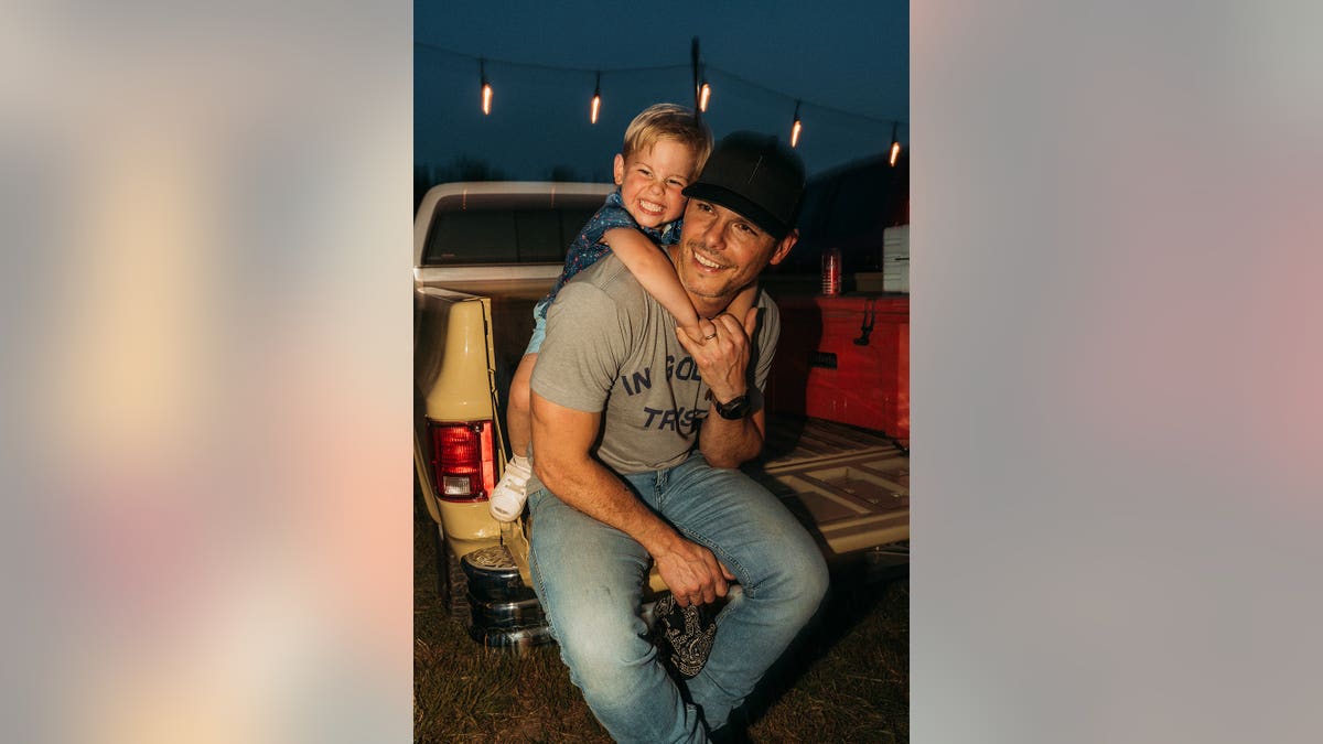 A smiling Maverick with his arms around his father Granger Smith.
