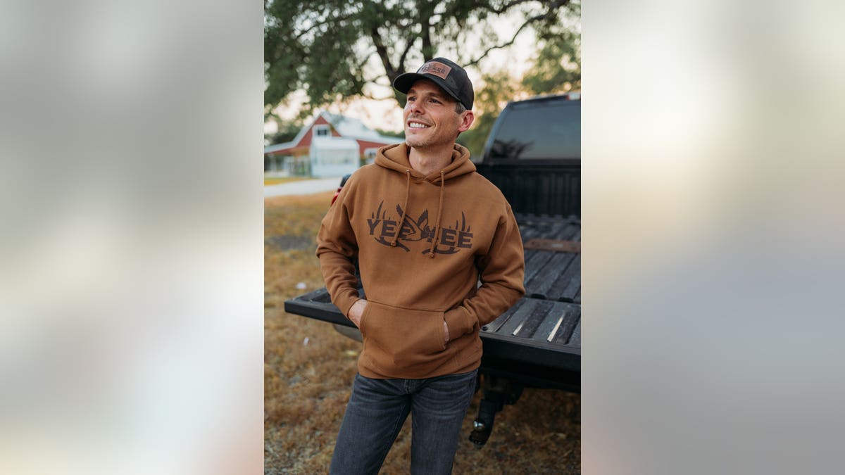 Granger Smith in a brown shirt smiling in front of his truck.