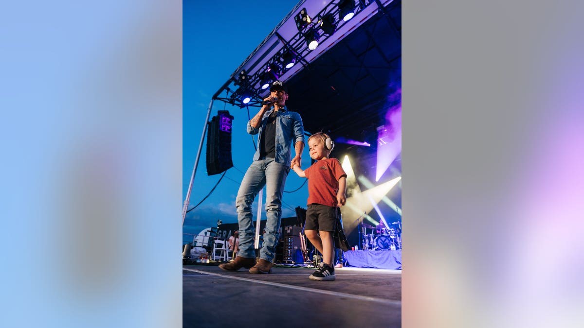 Granger Smith holding the hand of his son Maverick while performing on stage.