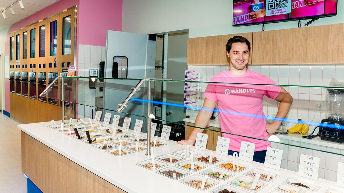 Neil Hershman smiles from behind the counter while wearing a pink 16 Handles shirt.