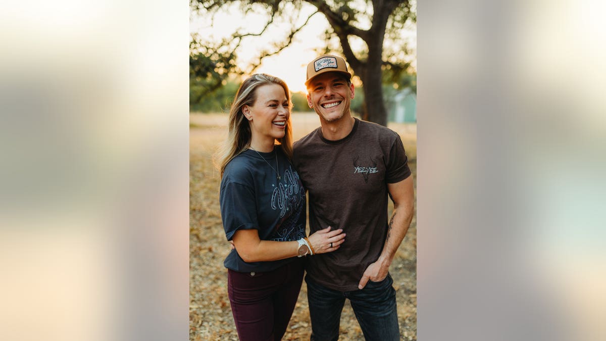Granger Smith and his wife Amber smile together in matching outfits outside.