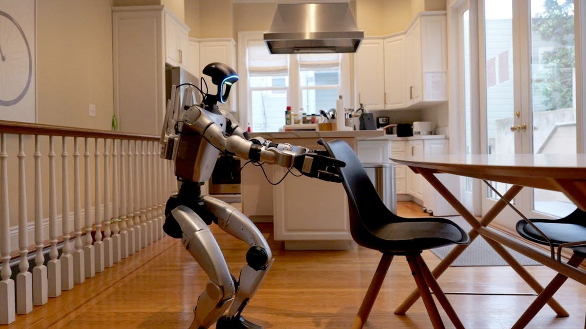 A humanoid robot pushes in a chair.