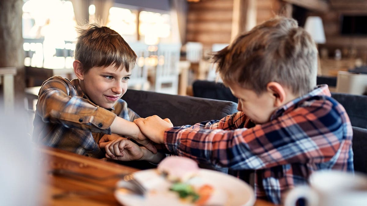 Two boys fighting and yelling while sitting at a restaurant table