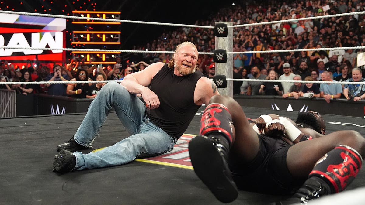 Brock Lesnar smiling while looking at Oba Femi lying on the mat during wrestling match