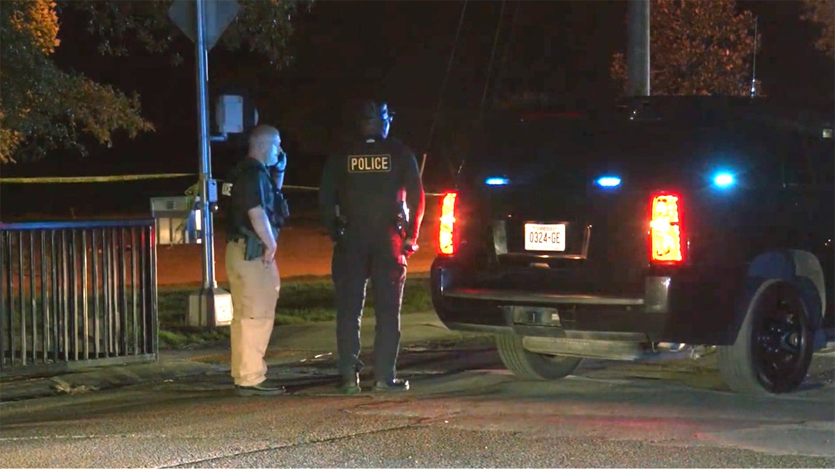 Police officers stand near a vehicle with flashing lights at a taped-off scene at night following a shooting in Brownsville, Tennessee.