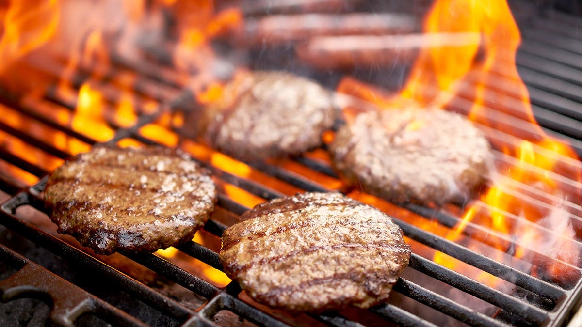 Close-up view of hamburgers and hot dogs cooking on a barbecue grill outdoors.