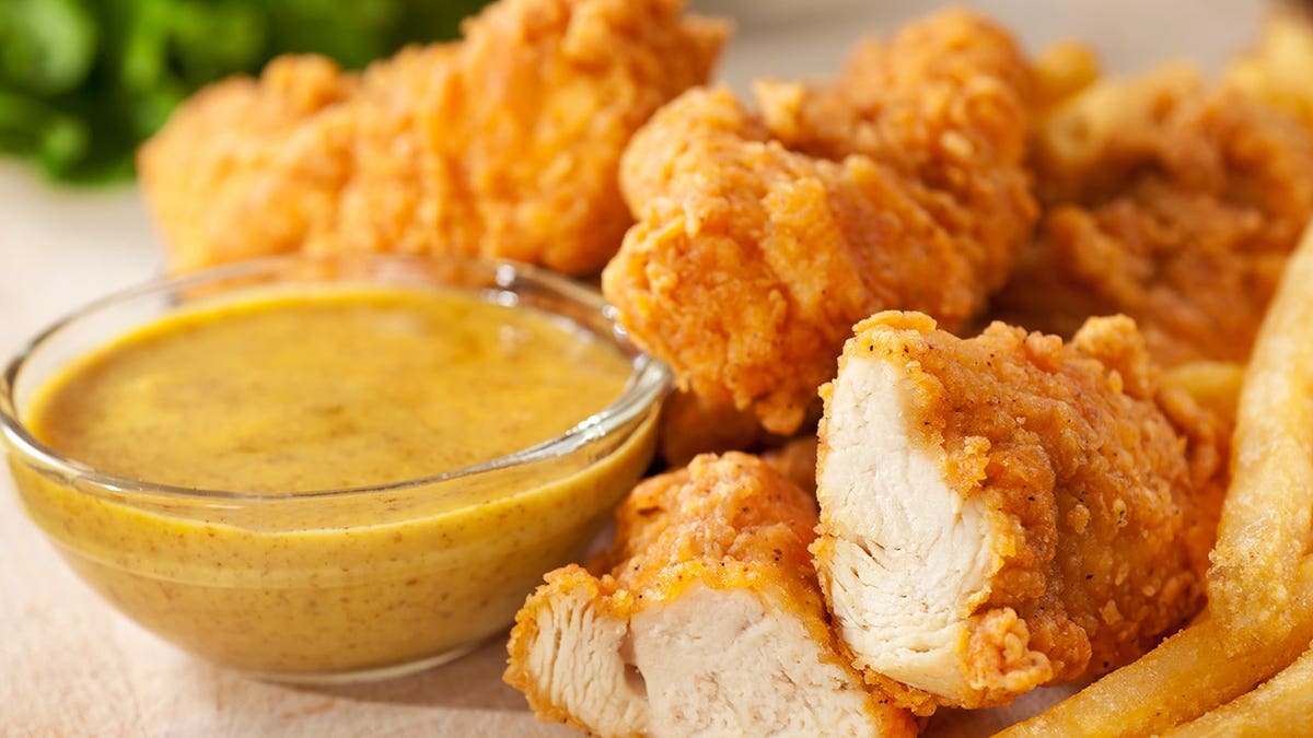 Chicken fingers served with honey mustard sauce and french fries on a plate
