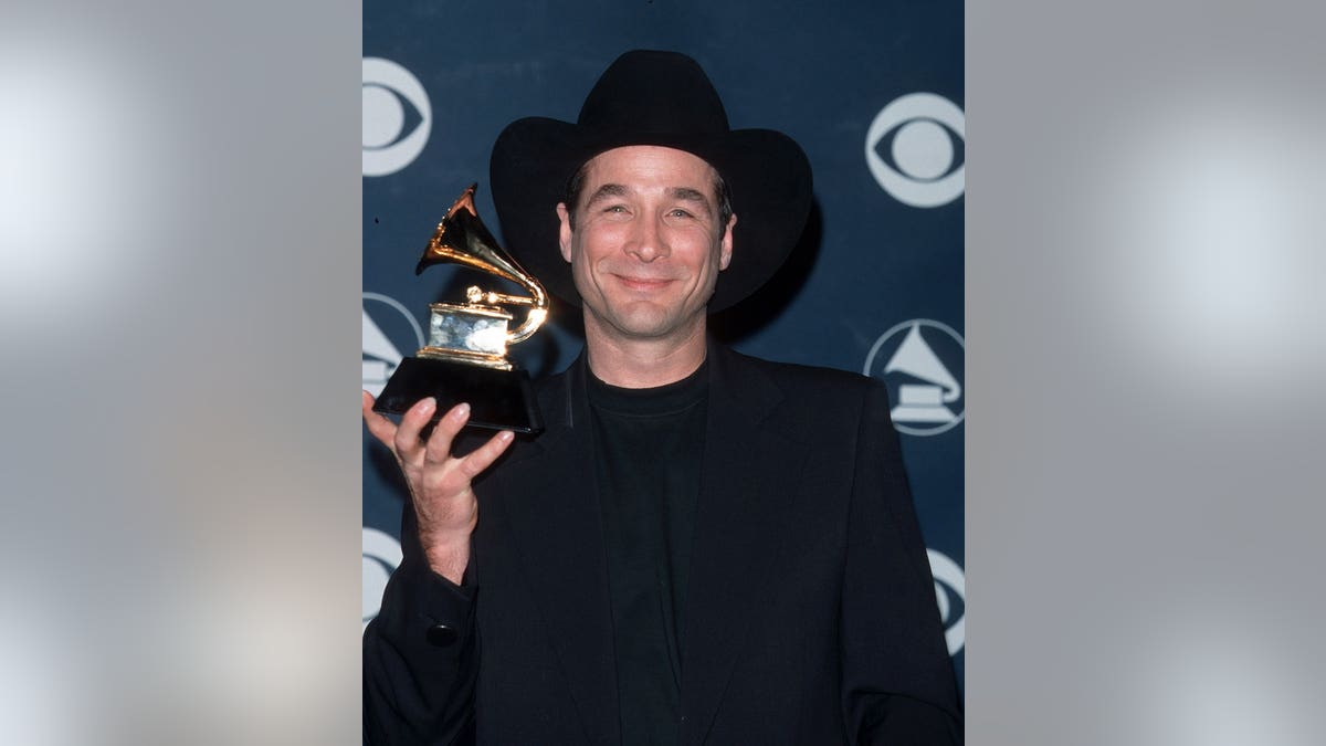 Clint Black standing and smiling in a black suit