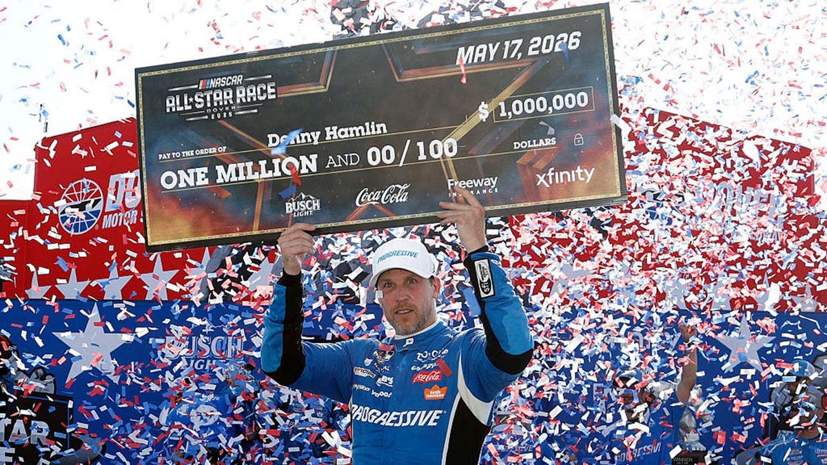 Denny Hamlin segurando um cheque de um milhão de dólares na pista da vitória em Dover Motor Speedway