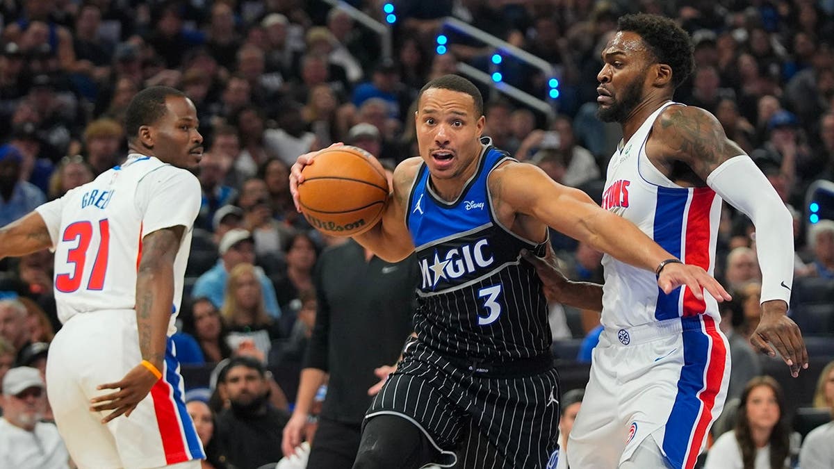 Orlando Magic guard Desmond Bane driving between Detroit Pistons defenders Javonte Green and Paul Reed during a basketball game