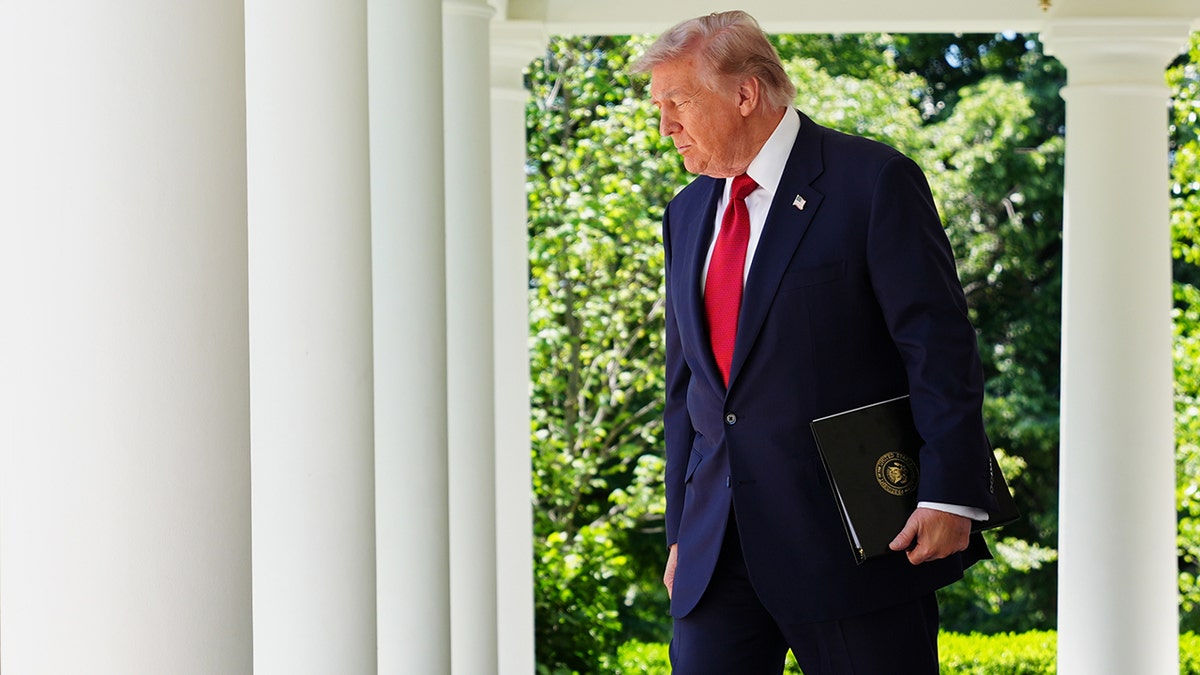Donald Trump walks through the White House Colonnade while holding a black folder.