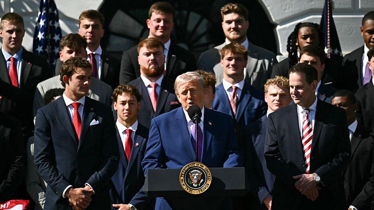 US President Donald Trump speaking with Indiana University football players behind him on the South Lawn at the White House