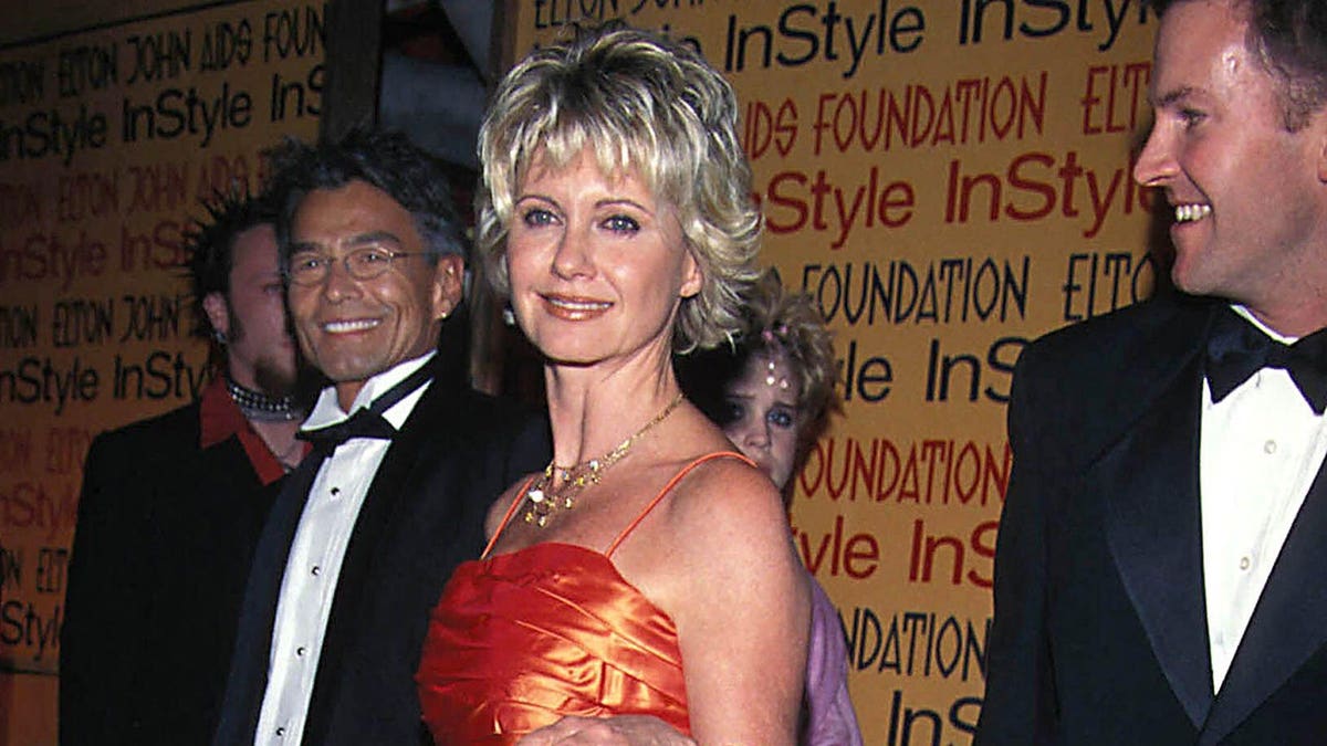 Patrick McDermott wearing glasses standing behind Olivia Newton John at Elton John Oscar party