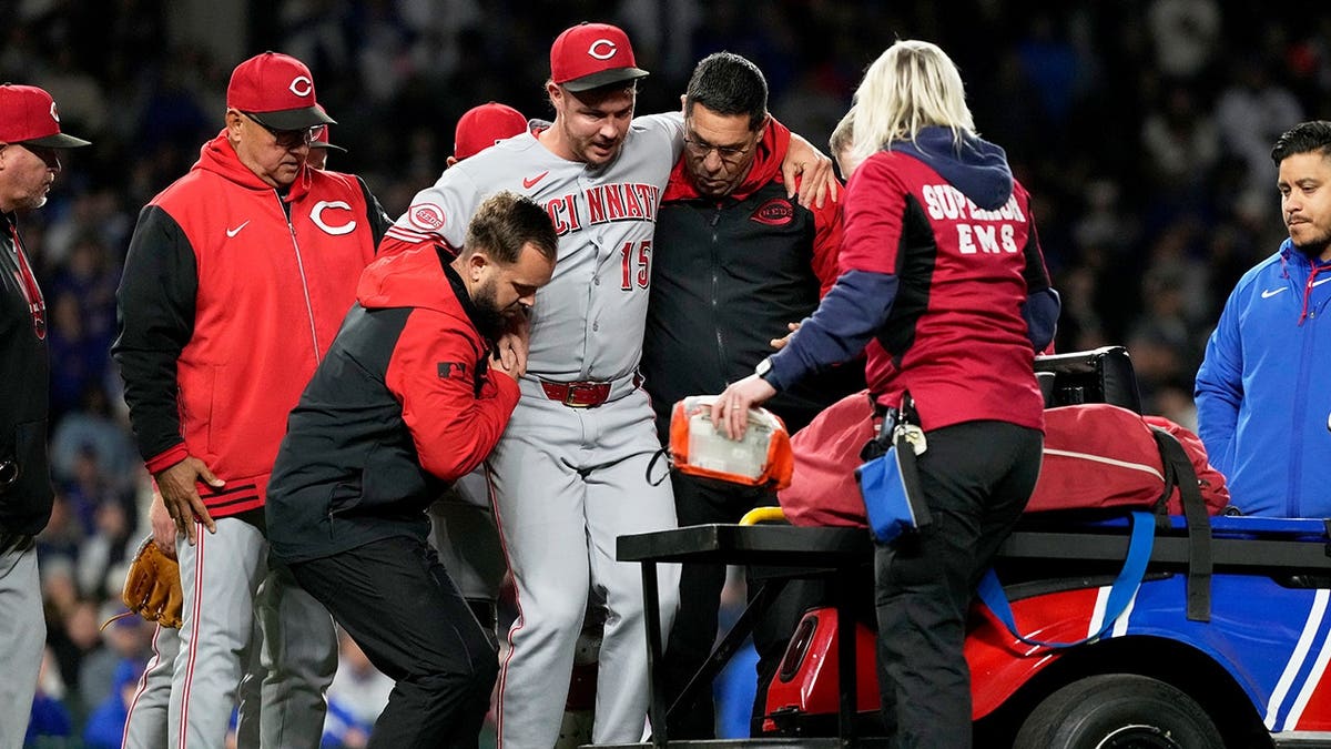 Cincinnati Reds relief pitcher Emilio Pagán being helped by trainers on baseball field