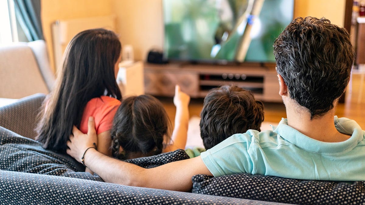 Parents and 2 children sitting connected sofa watching TV astatine home