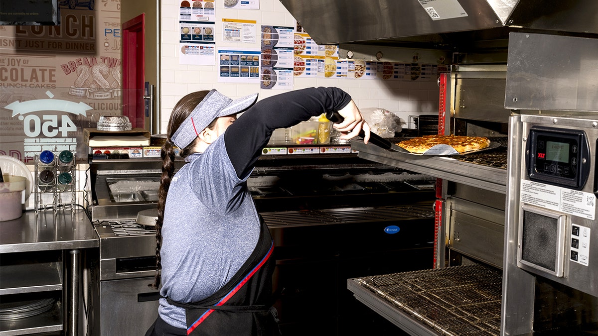 Female Domino's employee taking pizza out of oven