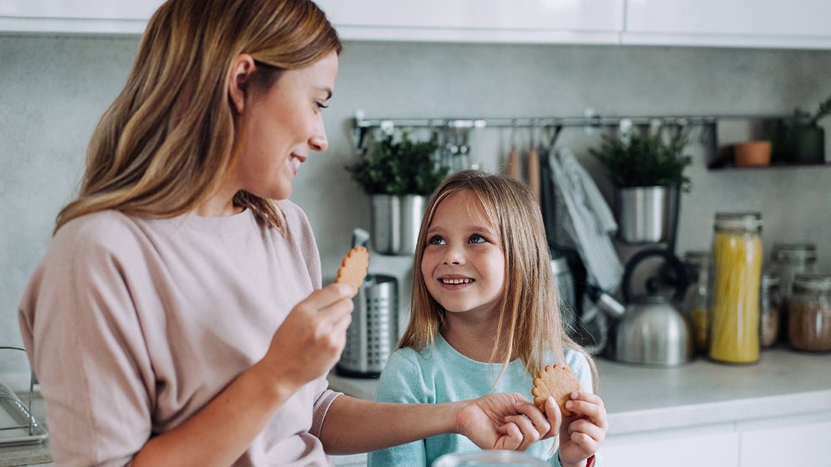Happy little girl eating a cookie at home with her mother