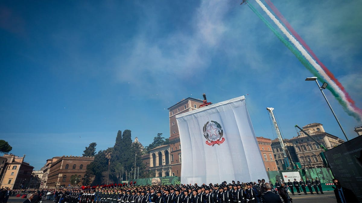armed forces in front of massive flag and below air show