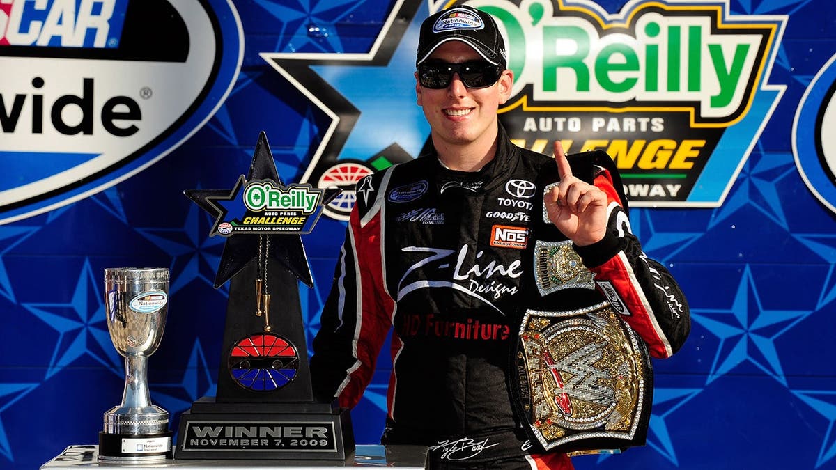 Kyle Busch posing in victory lane holding trophy and WWE championship belt replica