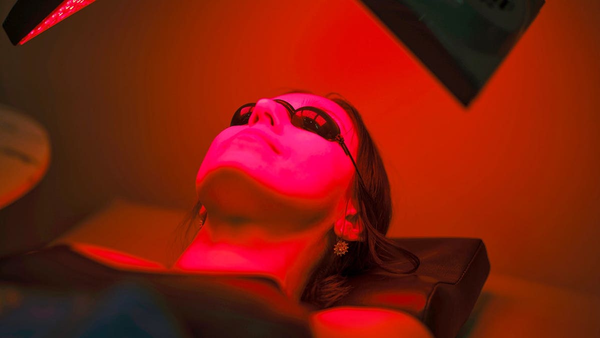A woman lying on a bed receiving LED red light therapy.