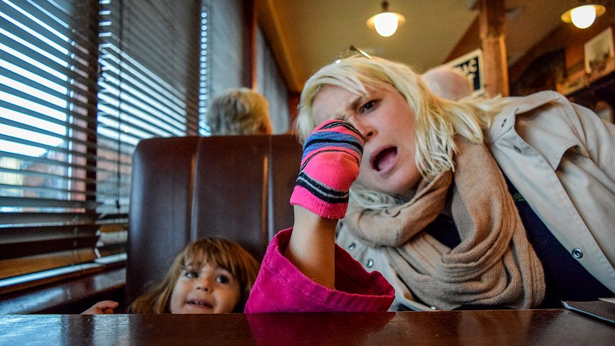 Little girl putting her foot on a restaurant table while her mother looks on
