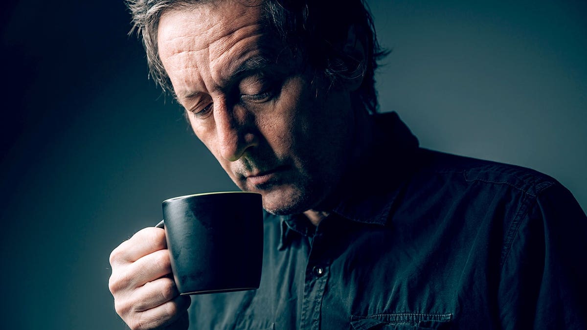 Mature man wearing black shirt drinking coffee from black cup