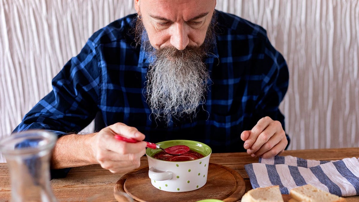 Pensive man with long beard eating beetroot soup