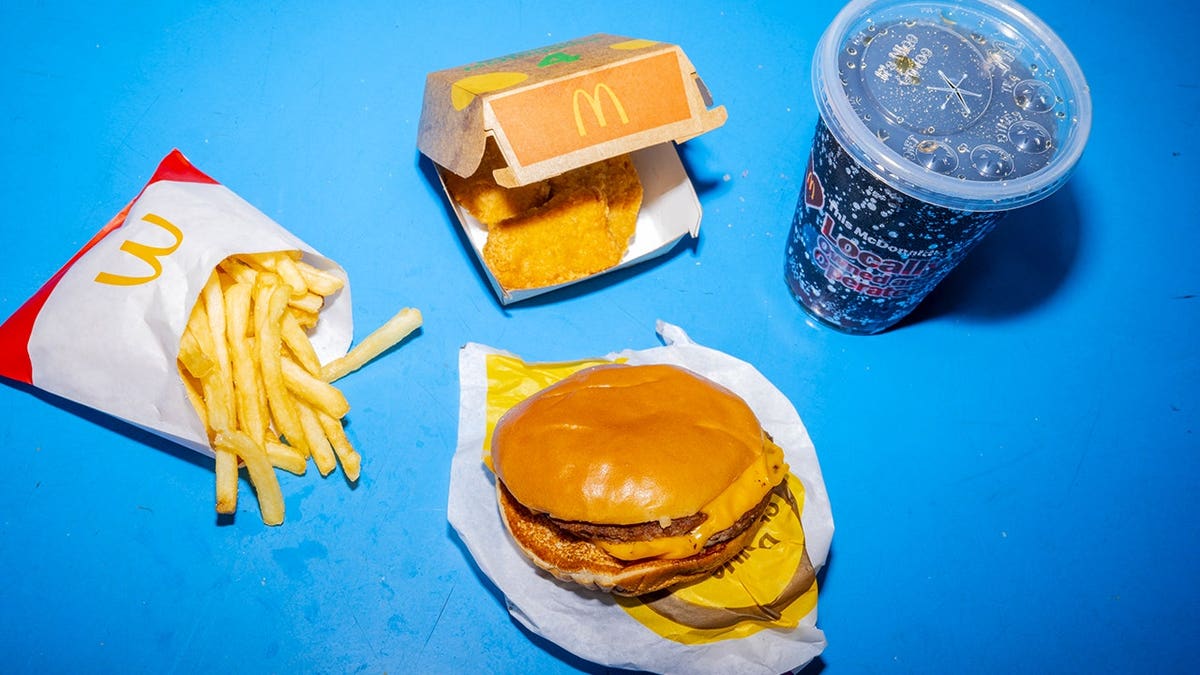 A McDonald's McDouble cheeseburger with fries, chicken nuggets, and a soft drink on a tray on a blue background.