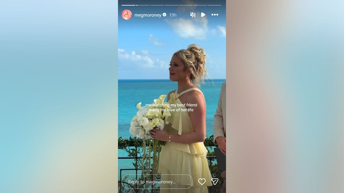 Megan Moloney wearing a yellow dress and holding a bouquet of flowers with the ocean in the background, May 2026.