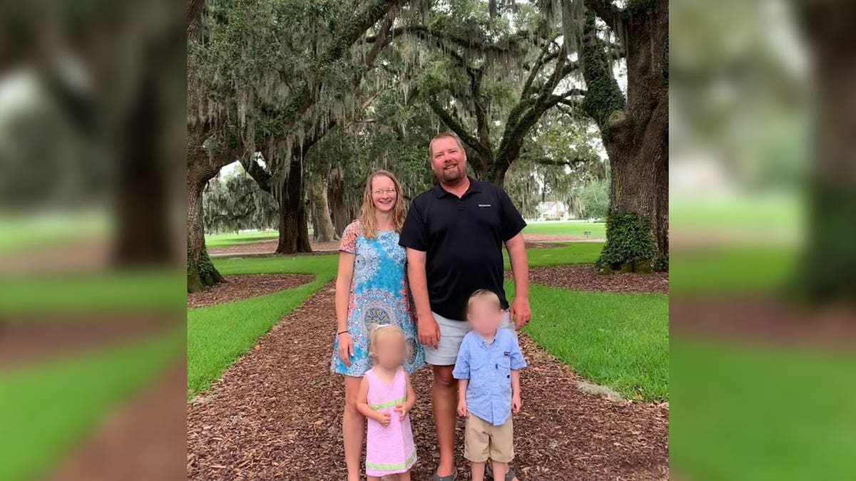 Una familia de cuatro miembros sonríe delante de unos árboles.