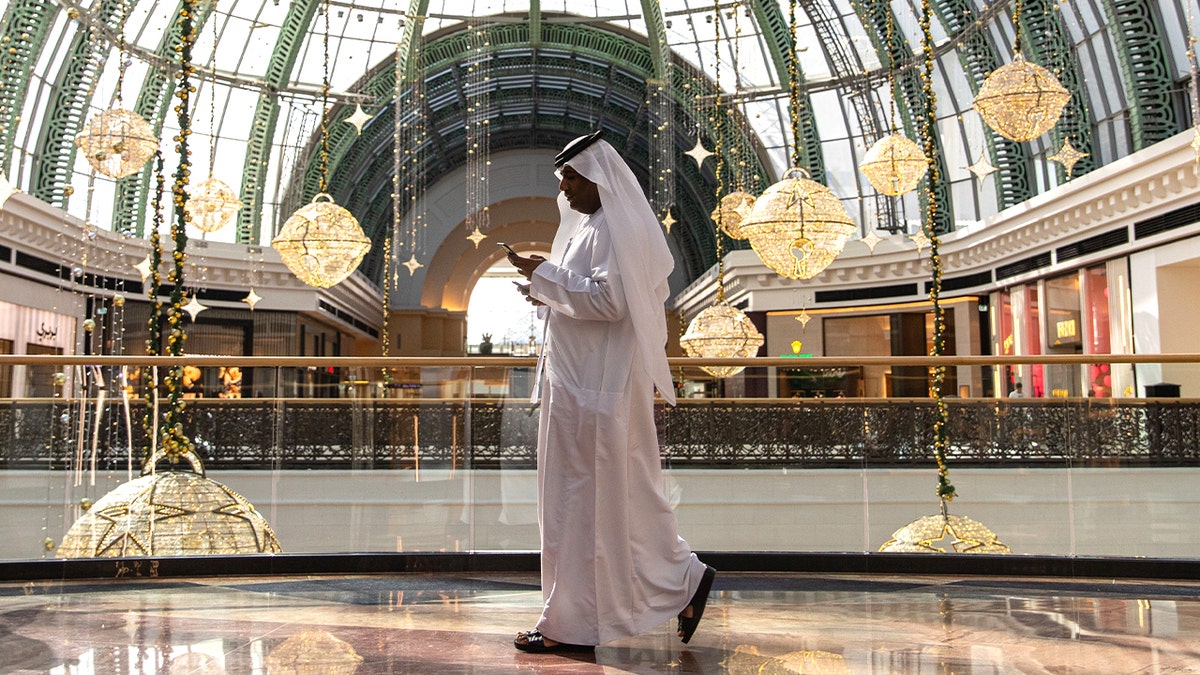 man in white keffiyah walks in shopping mall