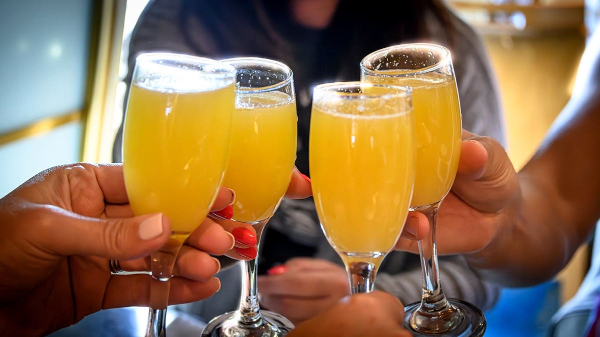 Um close de um grupo de amigos levantando copos de mimosa em um brinde no brunch.