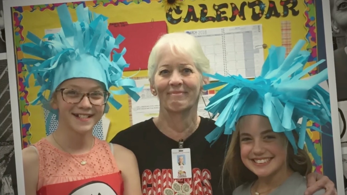 Katy Wells poses for a photo with two students wearing colorful blue paper mache hats