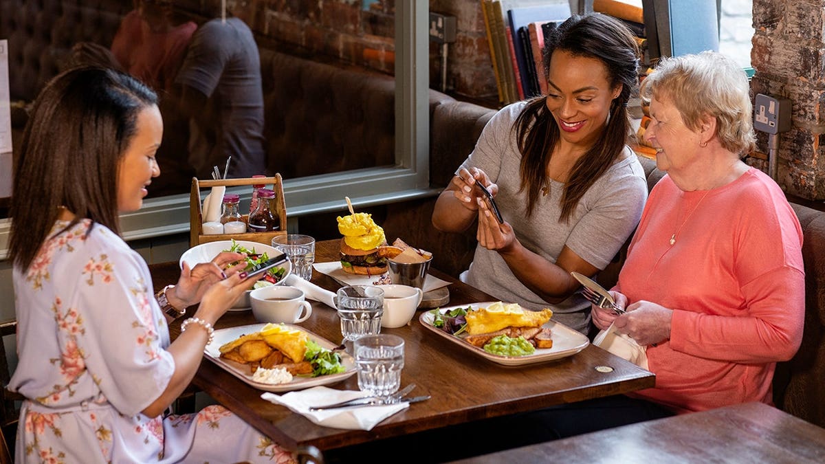 Uma mulher e suas duas filhas sentadas à mesa de um restaurante usando telefones celulares.