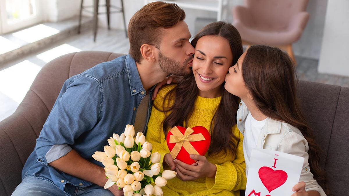 A mother receiving flowers and a handmade card from family members at home