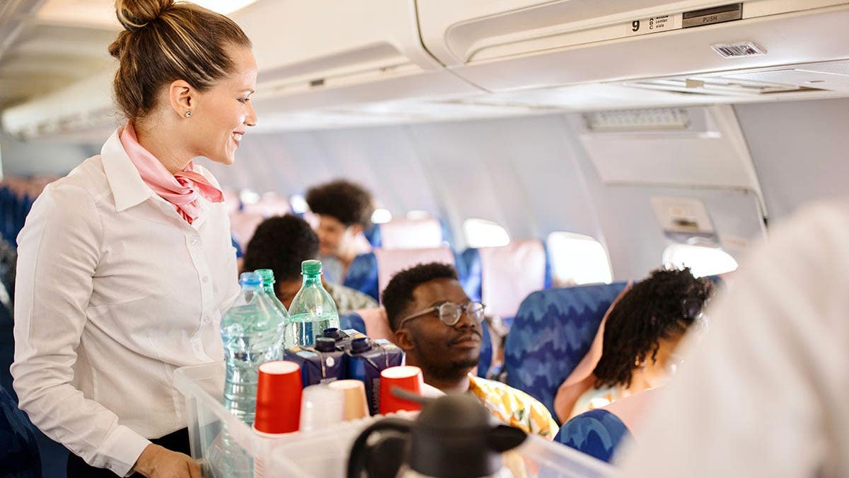 Cabin crew pushing service cart and serving a customer on an airplane during flight