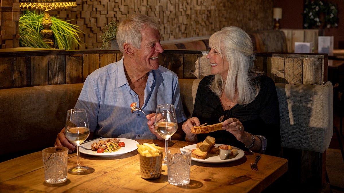 A cheerful older couple sitting across from each other at a restaurant table enjoying food